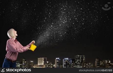 Young blond woman with yellow bucket in hands. Woman splashing stars from bucket