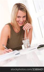 Young blond woman writing homework and having drink