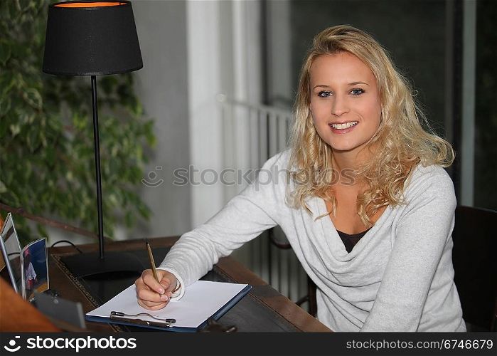 Young blond woman writing on clipboard