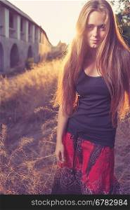 young blond women looking very seriously weared red skirt and black tank top. Against gold sunset light. Autumn time. Backlit