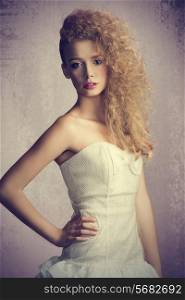 Young, blonde, beautiful girl with flufy, curly hairstyle. She is wearing white, gorgeous dress with a loop and colorful makeup.