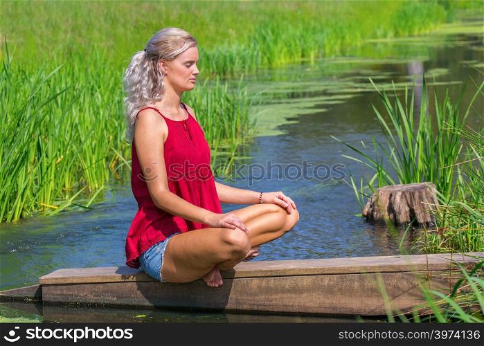 Young blonde caucasian woman meditates at river in nature