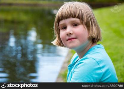 Young blonde dutch girl sitting at water of pond in park