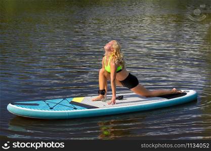Young blonde dutch woman stretches on SUP at water