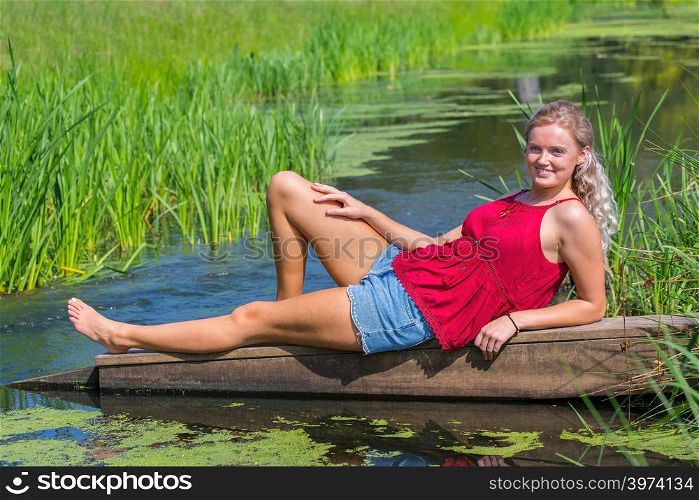 Young blonde european woman lying at water in nature