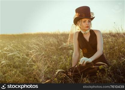 young blonde girl in a brown vintage dress and top hat in a feather grass