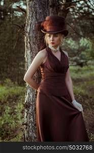 young blonde girl in a brown vintage dress and top hat in the forest
