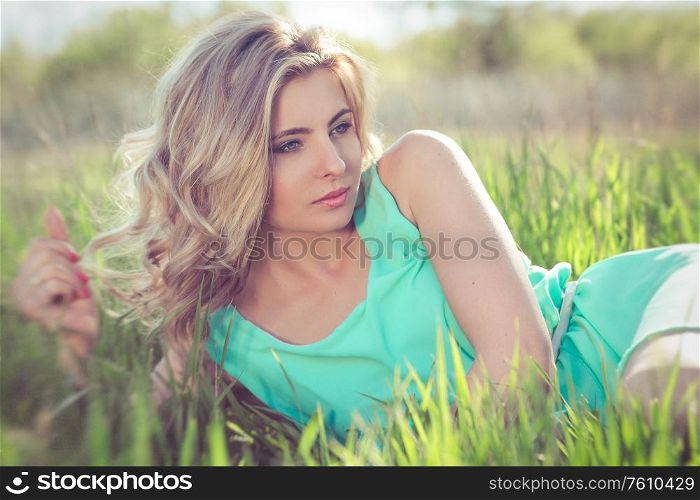 young blonde girl in a turquoise light dress walks in the spring garden