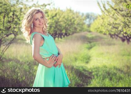 young blonde girl in a turquoise light dress walks in the spring garden