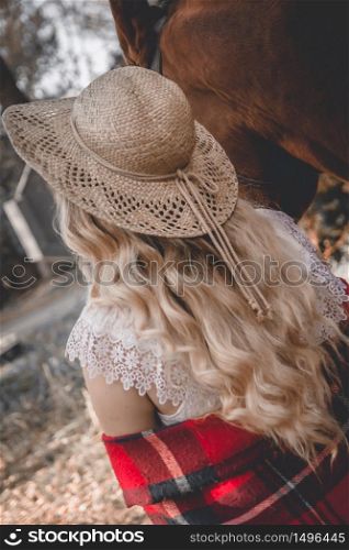 Young blonde girl in hat walking with horse.