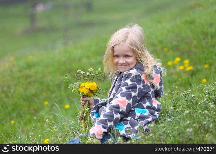 young blonde girl with bunch of dandelions on a green lawn