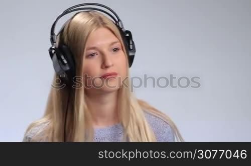 Young blonde girl with headphones listening to favorite music on white background. Happy attractive woman moving groovily to the beat, bobbing her head a little and smiling while listening to the upbeat song.