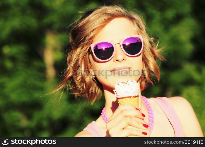 Young blonde hipster girl eating a delicious ice cream in summer hot weather in sunglasses have fun and good mood looking in camera and smiling.