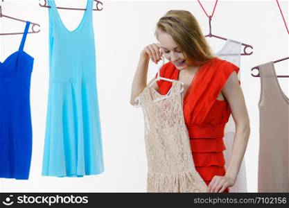 Young blonde long hair woman in clothes in shop or wardrobe choosing summer outfit, dresses hanging on clothing hangers, on white. Sale shopping fashion and style concept. Woman choosing clothes in shop