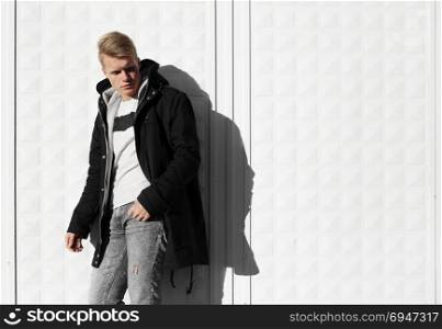 Young blonde man in autumn clothes standing near white wall. Young blonde man in autumn clothes standing near white wall.
