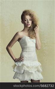 Young, blonde, pretty girl with curly and wild hairstyle. She is wearing white, gorgeous dress with a loop and colorful makeup.