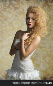 Young, blonde, pretty girl with curly hairstyle and romantic look. She is wearing white, gorgeous dress with a loop and colorful makeup.