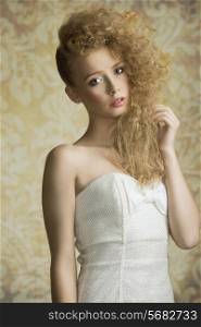 Young, blonde, pretty girl with curly hairstyle. She is wearing white, gorgeous dress with a loop and colorful makeup.