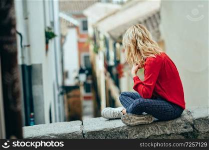 Young blonde tourist woman sitting outdoors looking a beautiful narrow street in Granada, Andalusia, Spain