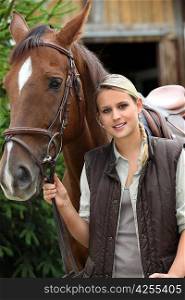 young blonde woman and a horse in front of a stable