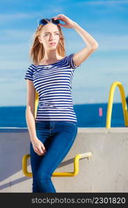 Young blonde woman casual style against stone wall sea in the background