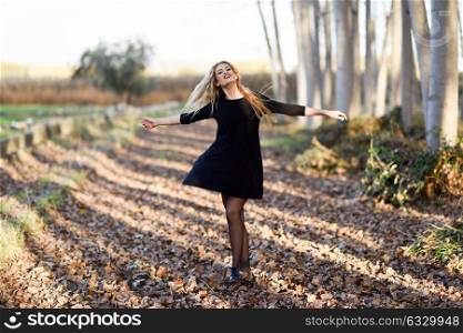 Young blonde woman dancing in poplar forest. Woman wearing black dress with flying hair