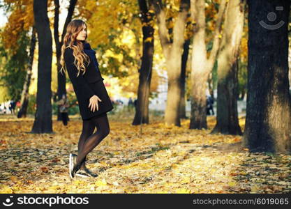 young blonde woman in autumn in park smiling wearing black coat and blue scarf