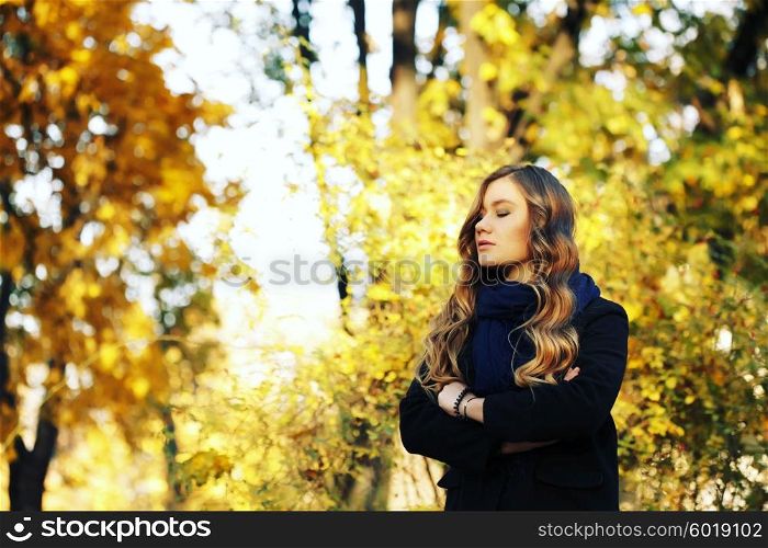 young blonde woman in autumn in park smiling wearing black coat and blue scarf