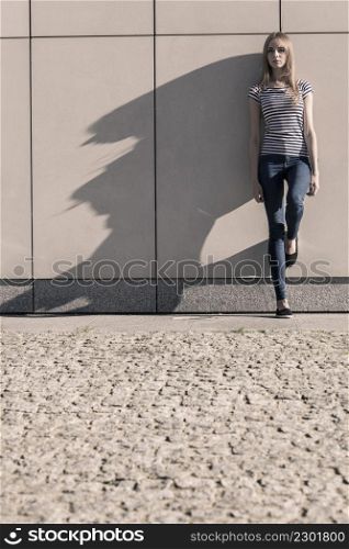 Young blonde woman in full length casual style against stone grunge wall