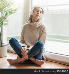 Young blonde woman in headphones listening to music and relaxing at home.
