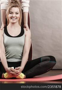 Young blonde woman in sportswear sitting on wooden floor indoor stretching legs with her female trainer. Training at home, being fit and healthy.. Woman in sportswear stretching legs with trainer