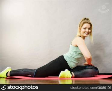 Young blonde woman in sportswear sitting on wooden floor indoor stretching legs. Training at home, being fit and healthy.. Woman in sportswear stretching legs