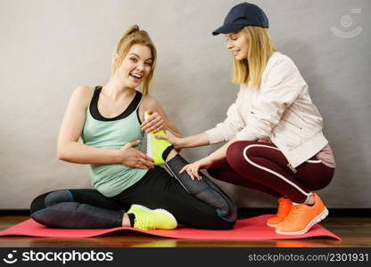 Young blonde woman in sportswear stretching body, working out with her female trainer. Training at home, being fit and healthy.. Woman in sportswear doing workout with trainer