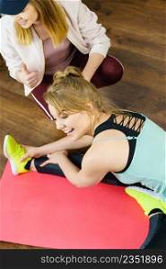 Young blonde woman in sportswear stretching body, working out with her female trainer. Training at home, being fit and healthy.. Woman in sportswear doing workout with trainer