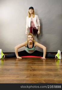 Young blonde woman in sportswear stretching body, working out with her female trainer. Training at home, being fit and healthy.. Woman in sportswear doing workout with trainer