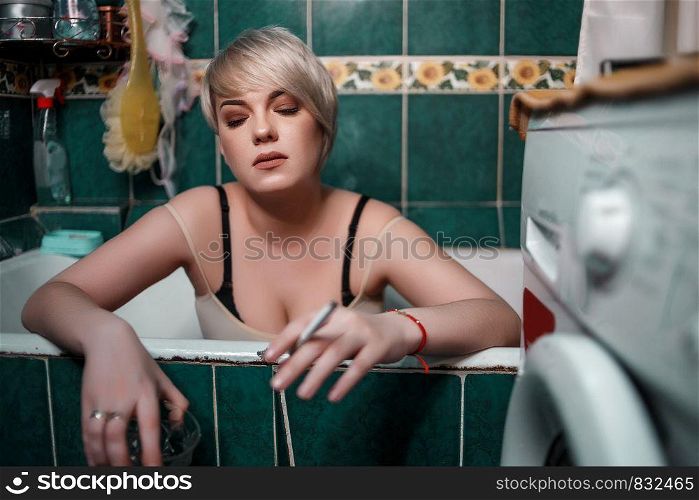 young blonde woman in the bathroom sitting drinking whiskey and Smoking cigarettes