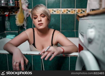 young blonde woman in the bathroom sitting drinking whiskey and Smoking cigarettes