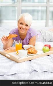 Young blonde woman is having breakfast in the bedroom
