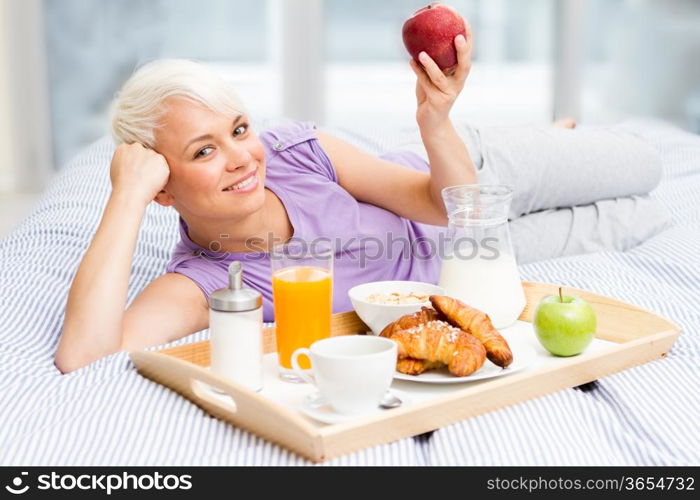 Young blonde woman is having breakfast in the bedroom