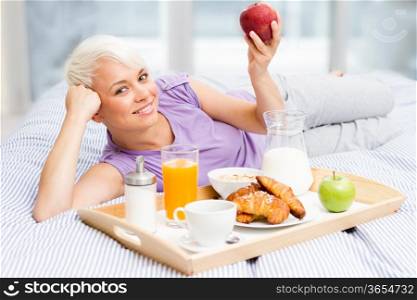Young blonde woman is having breakfast in the bedroom