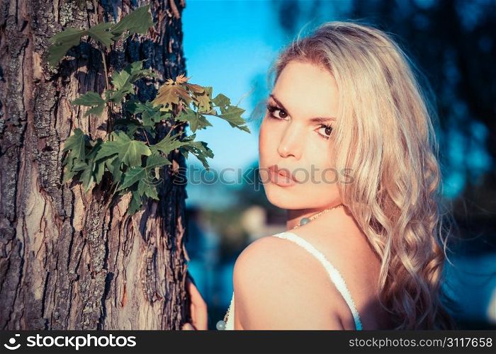 Young Blonde Woman next to a tree with a blue sky in the background