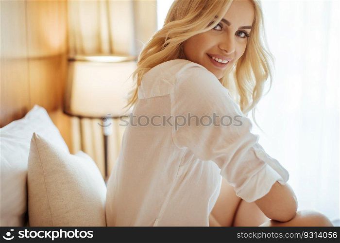 Young blonde woman on the bed in the room looks happy and satisfied