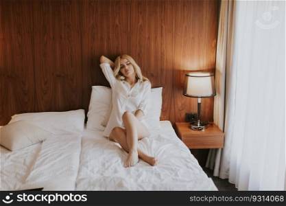 Young blonde woman on the bed in the room looks happy and satisfied