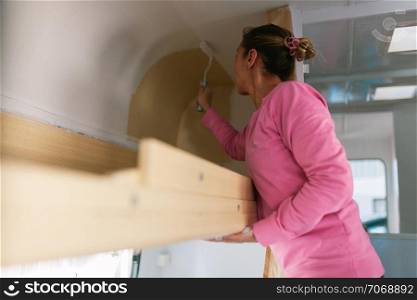 Young blonde woman painting and restoring caravan