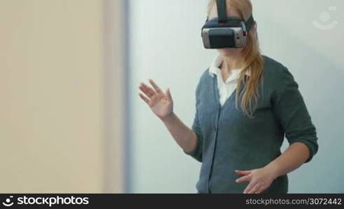 Young blonde woman playing game using VR-helmet for smart phones. Augmented reality device allows to deep into virtual space