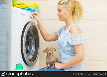 Young blonde woman setting washing clothes laundry machine knob, choosing program. Household duties concept.. Woman setting washing machine