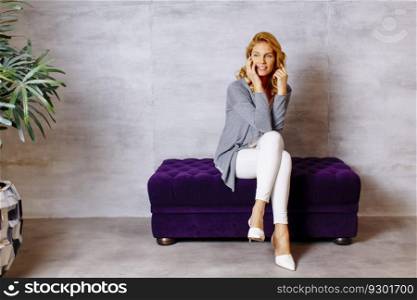 Young blonde woman sitting on a purple sofa using a mobile phone
