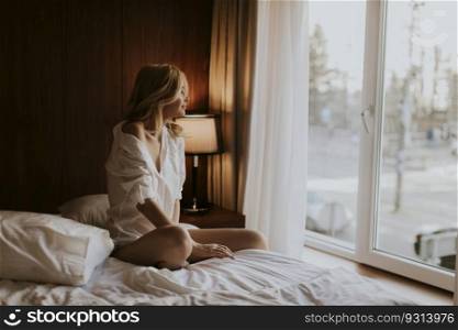 Young blonde woman sitting on the bed in the room looks melancholy