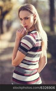 Young blonde woman standing in the street. Beautiful girl in urban background wearing striped dress and black tights. Female with straight hair.