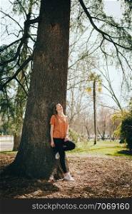 Young blonde woman supported on a tree with black jeans